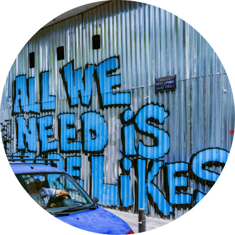 Image of a corrugated iron wall with blue graffiti reading "All we need are more likes"